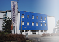 Siedziba firmy Kontakt Simon z niebieską fasadą i flagą firmową przed budynkiem